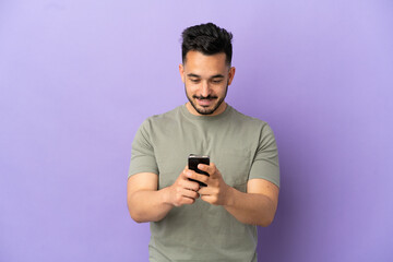 Young caucasian man isolated on purple background sending a message with the mobile