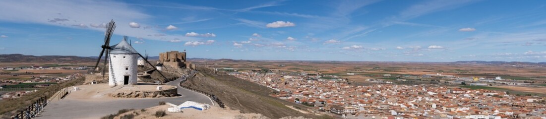 Panoramic view of the old windmills and the Castillo de la Muela located on top of a hill in the town of Consuegra located at the foot of the mountain in the province of Toledo, Spain - obrazy, fototapety, plakaty