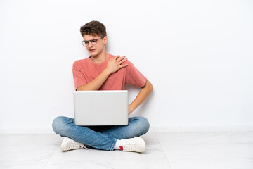 Teenager Russian man holding pc sitting on the floor isolated on white background suffering from pain in shoulder for having made an effort