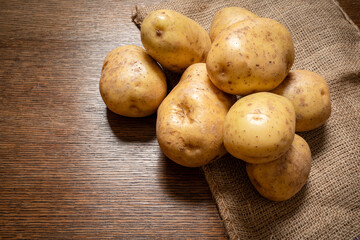 A pile of raw, uncooked big British baking potatoes are placed on a wooden worktop.