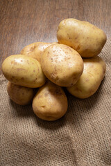 A pile of raw, uncooked big British baking potatoes are placed on a wooden worktop. Upright image.