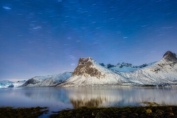 Fototapeta na wymiar Mountains and starry night sky, Senja islands, Norway. Reflection on the water surface. Winter landscape with night sky. Norway travel image