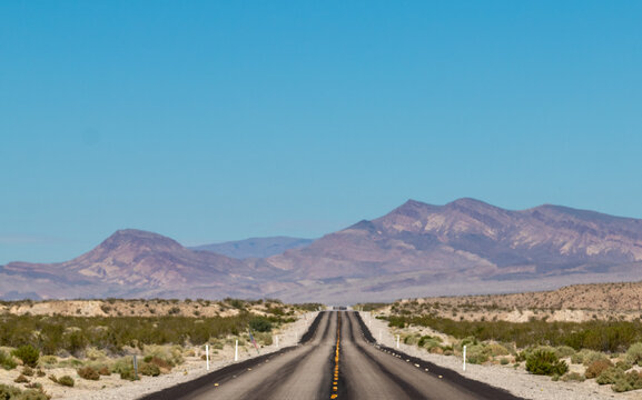 endless road in the desert, route 93, image shows a endless asphalt road in the navada desert, surrounded by untouched land and sand, with distant mountain views and rocks, taken october 2023