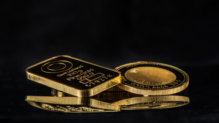 Gold bars and 2 troy ounce gold coin on a black mirror background. Selective focus.