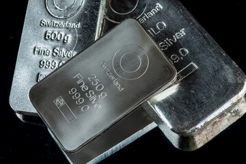 Several silver bars of different weight on a dark mirror surface. Selective focus.