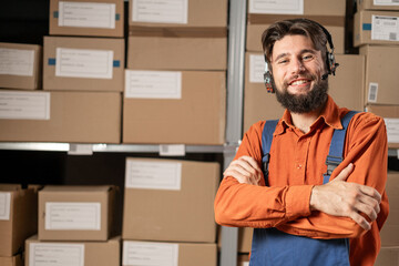 Male worker wearing headset in logistics distribution warehouse looking at camera and smiling