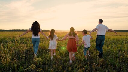Parents, children run hand in hand across field at sunset. Family, children play, run together, travel in nature. Mom, dad, children run through meadow, family dream of fly. Father mother son daughter