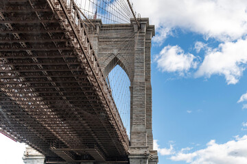 Fototapeta premium Low angle view of one of the suspension towers of the Brooklyn Bridge, New York City, NY, USA with view of bridge deck against a white clouded blue sky