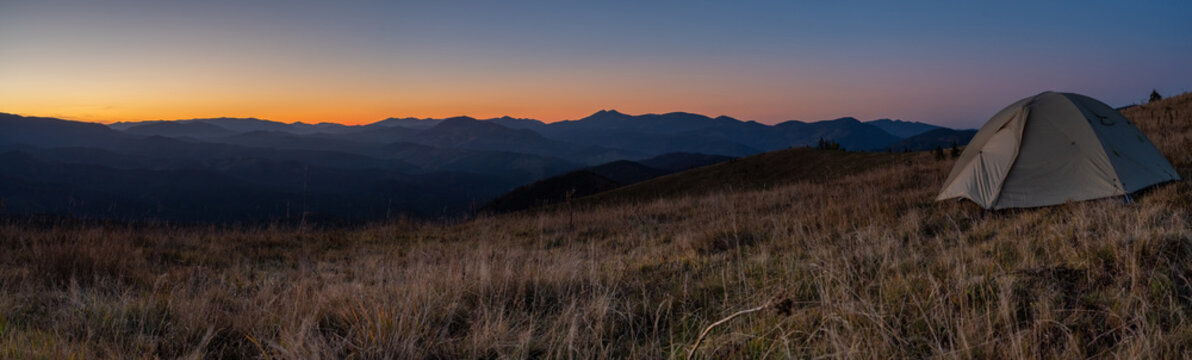 Panorama of landscape with a tourist tent. Mountain peaks Mountain range. Tourism and hiking. Panorama of sunset in the mountains.
