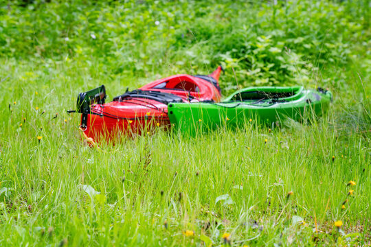 Two intentionally blurred kayaks - red and green ones are on the green grass. Close up low level photo. Foreground grass in focus