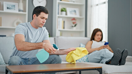 Obraz premium Beautiful couple cleaning while girlfriend using smartphone at home