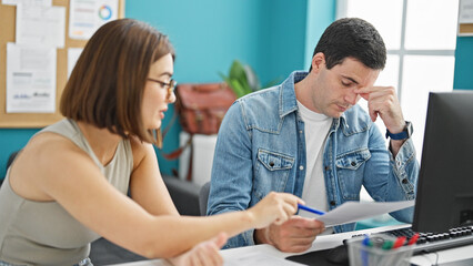 Two workers man and woman sitting on table reading document looking upset at the office