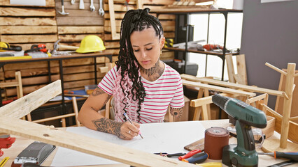 Confident hispanic amputee woman, sitting and drawing creative carpentry designs at her...