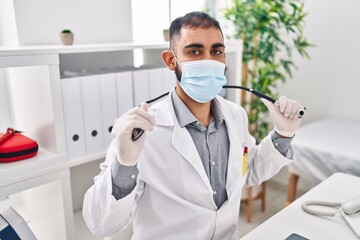Young hispanic man doctor wearing medical mask holding stethoscope at clinic