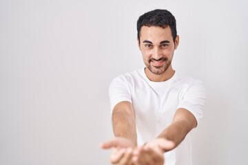 Handsome hispanic man standing over white background smiling with hands palms together receiving or...