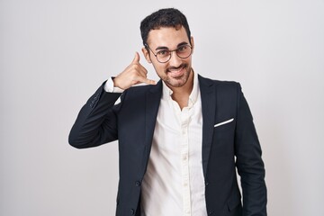 Handsome business hispanic man standing over white background smiling doing phone gesture with hand and fingers like talking on the telephone. communicating concepts.