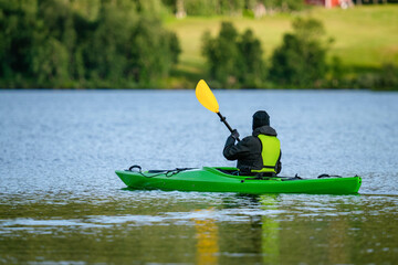 Mature women in green safety life jacket kayaking in green kayak. Rear side photo on still water...