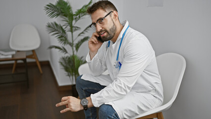 Focused young hispanic man, a serious doctor in uniform with stethoscope, deeply immersed in thinking as he scans x-ray in the clinic's waiting room, doubt etched in his expression.