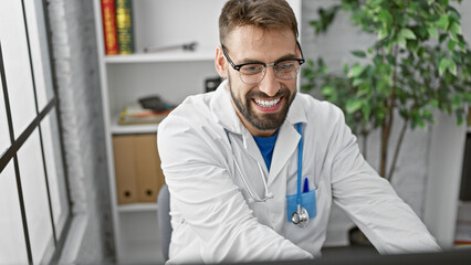 Fototapeta premium Confident young hispanic man working as a doctor at the clinic, smiling behind the computer