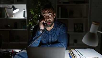 Bearded young hispanic man concentrating, having serious talk on phone while sitting at office's...