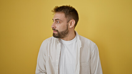Chill yet serious, young hispanic guy with a beard giving a side glance, exuding a cool, relaxed vibe. solo portrait, cutout over yellow wall - a casual lifestyle statement.