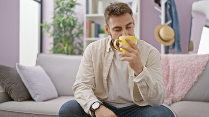 Handsome young hispanic man relaxes on sofa at home, enjoying the aromatic smell of morning coffee...