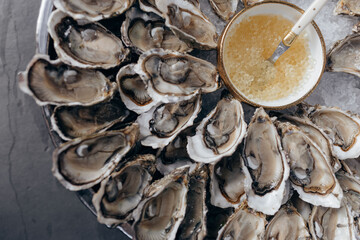 Close-up of fresh open oysters with sauce on round platter in restaurant. Seafood. Healthy 