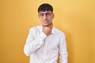 Young hispanic man standing over yellow background touching painful neck, sore throat for flu, clod and infection
