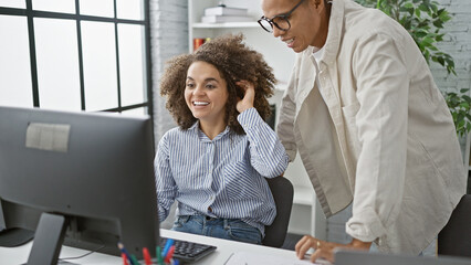 Two team partners, a man and a woman, enjoy working together at the office, smiling confidently while using a computer in indoor professional surroundings