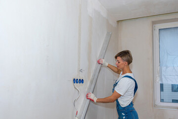 Renovation at home. Woman makes repairs in new apartment. Worker levels walls with building water...