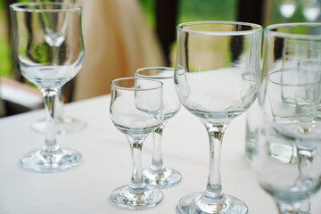 Empty wine glasses and shot glasses on a table with a white tablecloth.