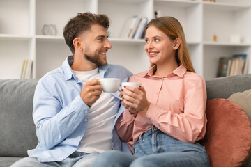Young couple in love drinking tea sitting on sofa indoors