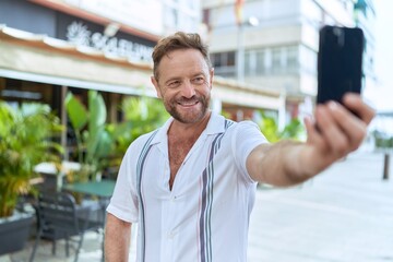 Middle age man smiling confident making selfie by the smartphone at coffee shop terrace