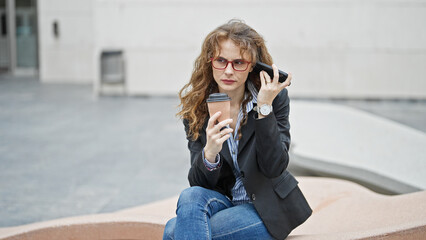 Young woman business worker listening to voice message by smartphone holding coffee at street