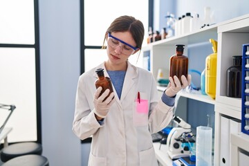 Naklejka na ściany i meble Young blonde woman scientist holding bottles with liquid at laboratory