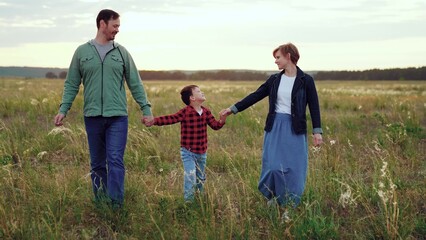Loving parents hold son hands in field with growing plants in cloudy weather