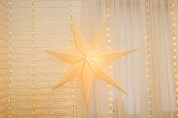 Christmas star on golden lights background on wall in living room. Large paper star glows against...