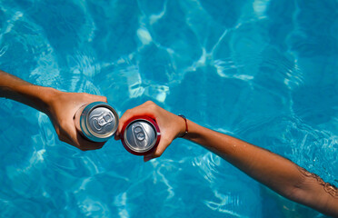 Pool party on summer holiday. Close-up of hands with cans of beer or refreshing drinks in the...