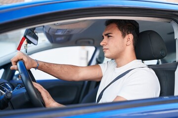 Young hispanic man stressed driving car at street