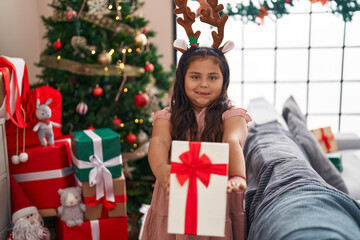 Plus size hispanic girl holding gift standing by christmas tree at home