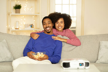 African couple enjoys movie sharing hugs lounging with popcorn indoor