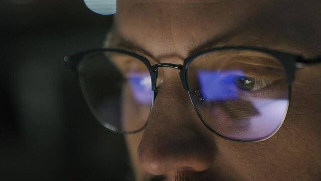 Close up male eyes in glasses eye strain problem medicine night dark man businessman developer computer programmer business man looking at screen blue laptop display monitor reflection in eyeglasses