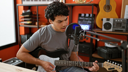 Young latin man musician singing song playing electrical guitar at music studio