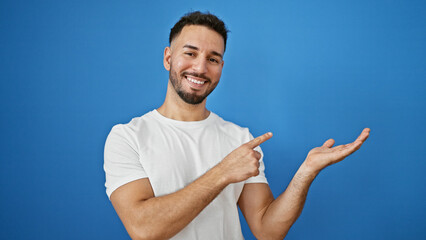 Young arab man smiling pointing to the side presenting over isolated blue background