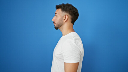 Young arab man looking to the side with serious expression over isolated blue background