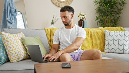 Young arab man using laptop sitting on sofa at home