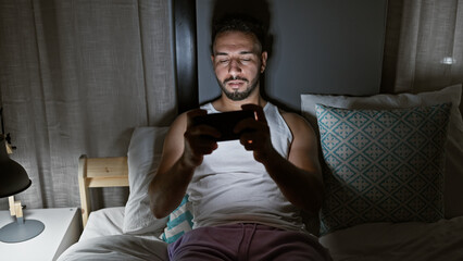 Young arab man playing video game sitting on bed at bedroom