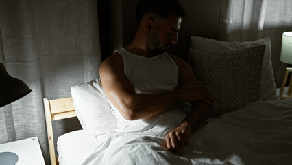 Young arab man sitting on bed scratching arm for itchy at bedroom - obrazy, fototapety, plakaty