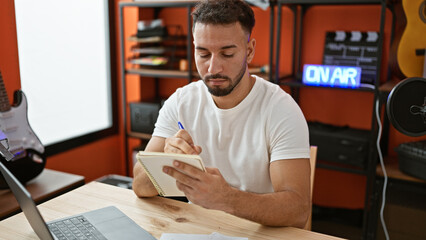 Young arab man musician composing song writing on notebook at music studio