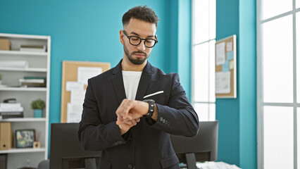 Young arab man business worker looking watch with serious face at the office